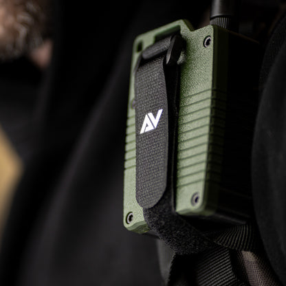 A close-up of a green Atlavox M1 radio, secured to backpack strap on chest.